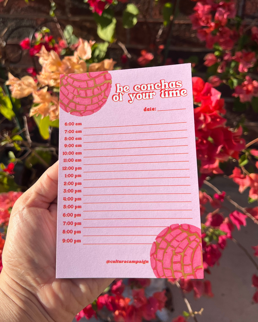 Pink notepad with time slots held in front of flowers