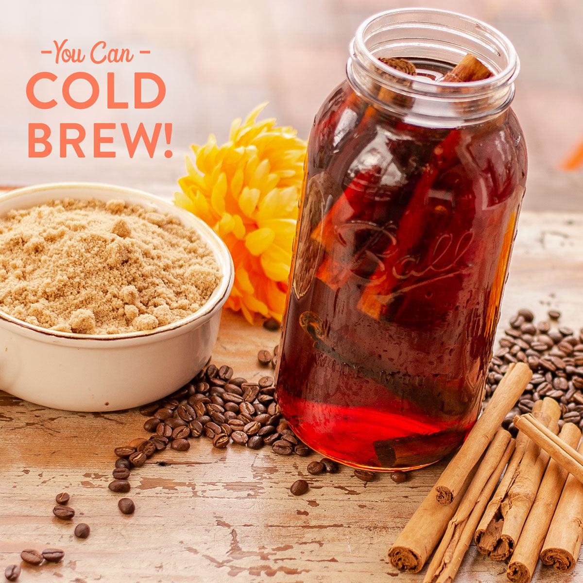 Cold brew coffee preparation with a jar, sugar, coffee beans, and cinnamon on a wooden surface.