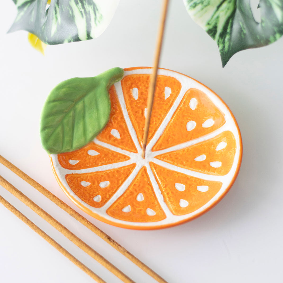 Decorative incense holder shaped like an orange slice with a leaf on a white background