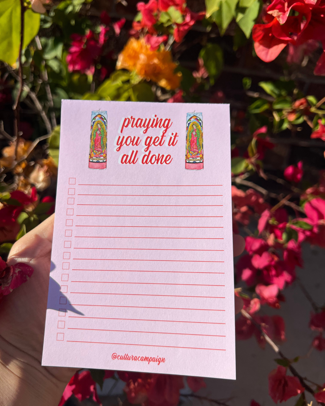 Notepad with 'praying you get it all done' text held in front of flowers
