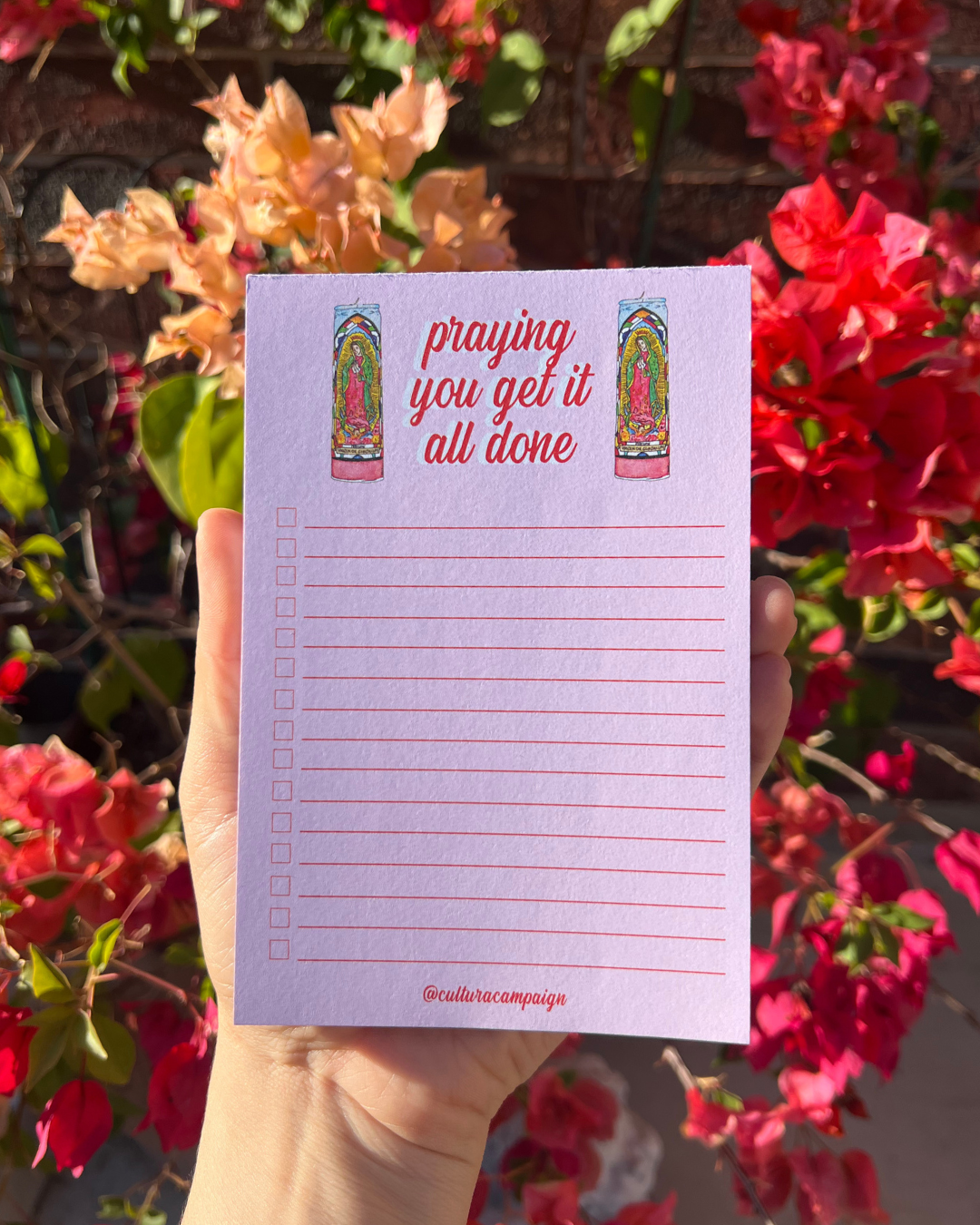 Notepad with 'praying you get it all done' text held in front of flowers