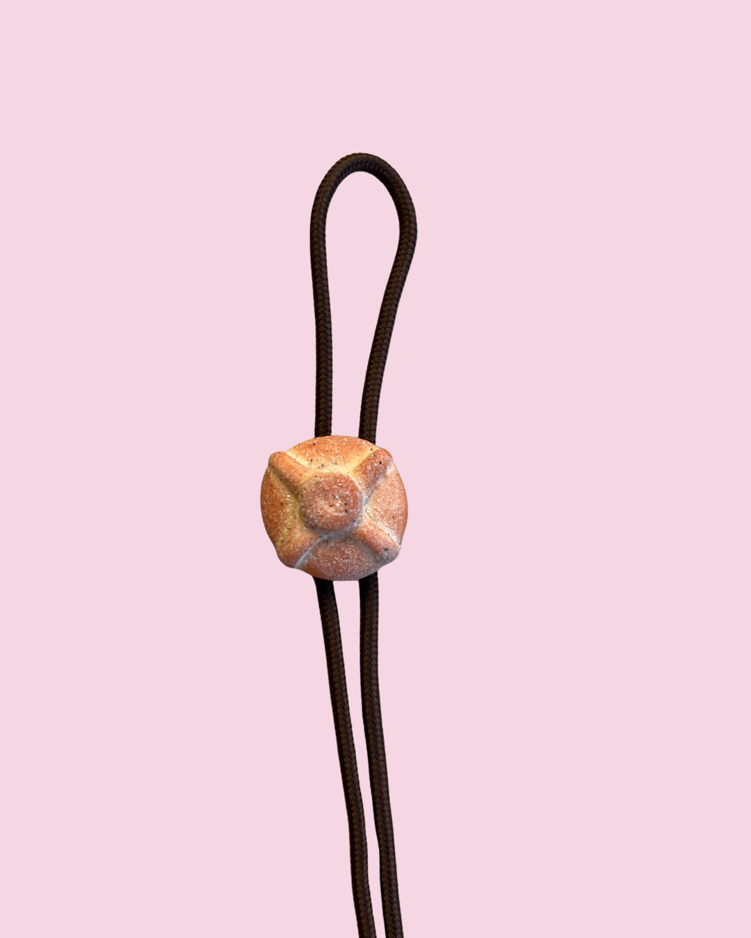Bolo tie with a textured pan dulce clasp on a pink background