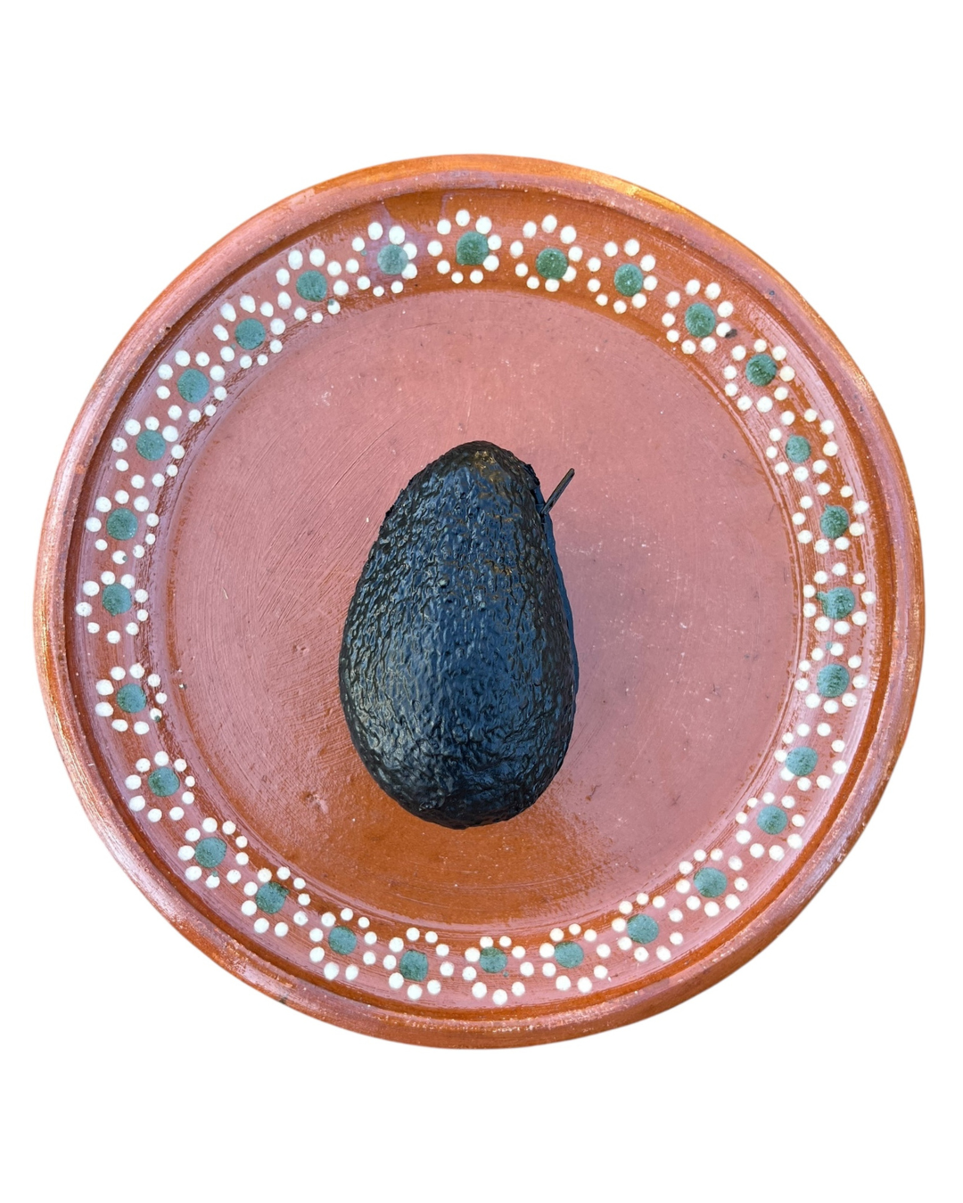 Avocado coin purse on a decorative ceramic plate with a pink center and brown rim.