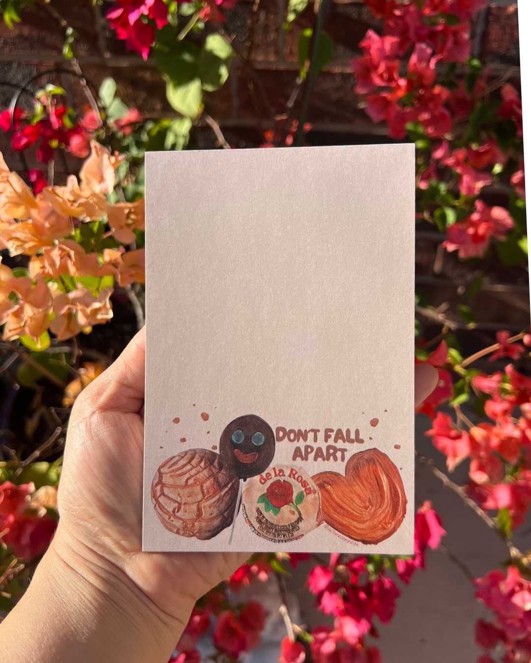 Notebook with pan dulce illustrations and text held in front of a floral background
