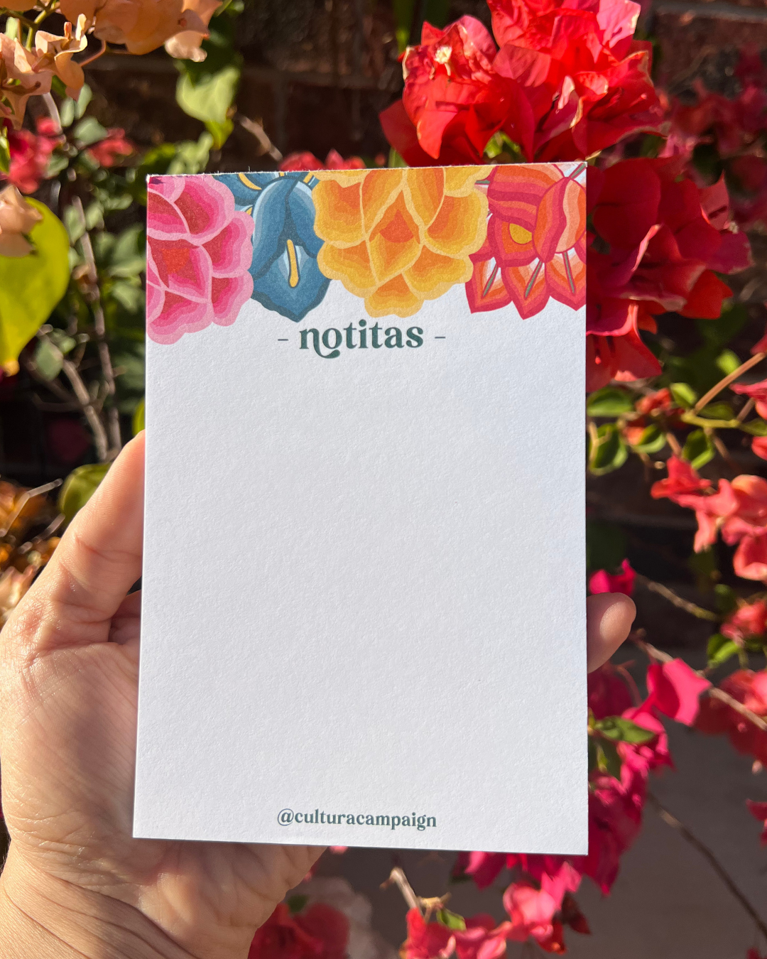 Hand holding a colorful notepad with 'notitas' title amidst flowers