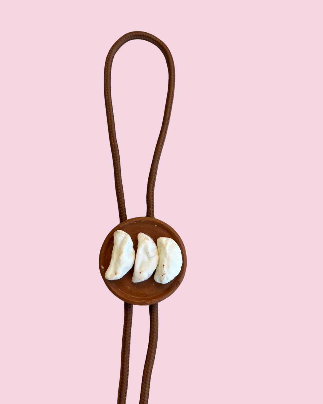 Bolo tie with three tortillas on plate on a pink background