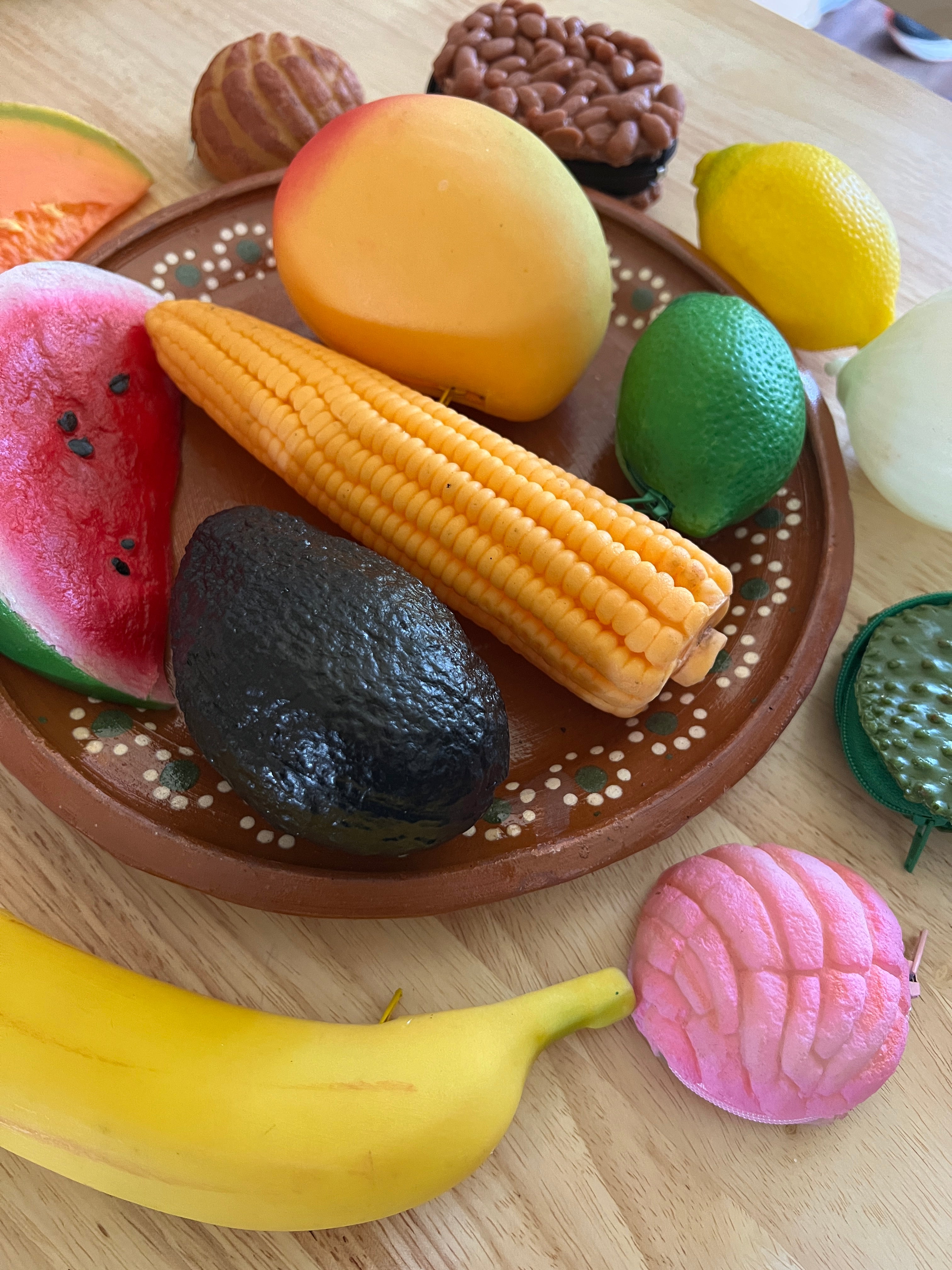 A collection of colorful handmade coin purses designed to look like various fruits and vegetables displayed on a brown plate.