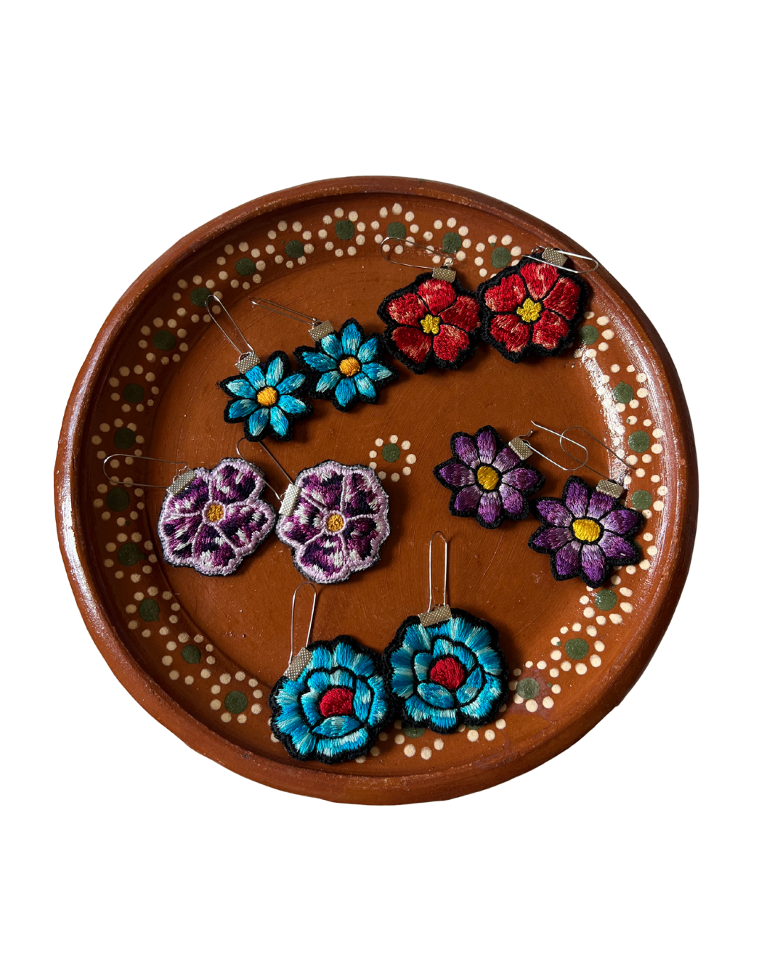 Set of colorful flower-shaped earrings on a decorative wooden plate.