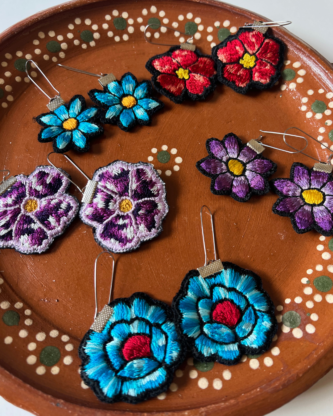 Colorful flower-shaped earrings on a decorative brown plate