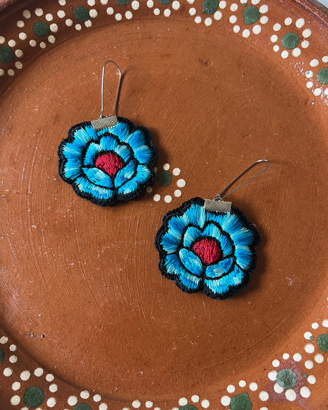 Blue embroidered flower earrings on a barro plate with decorative patterns