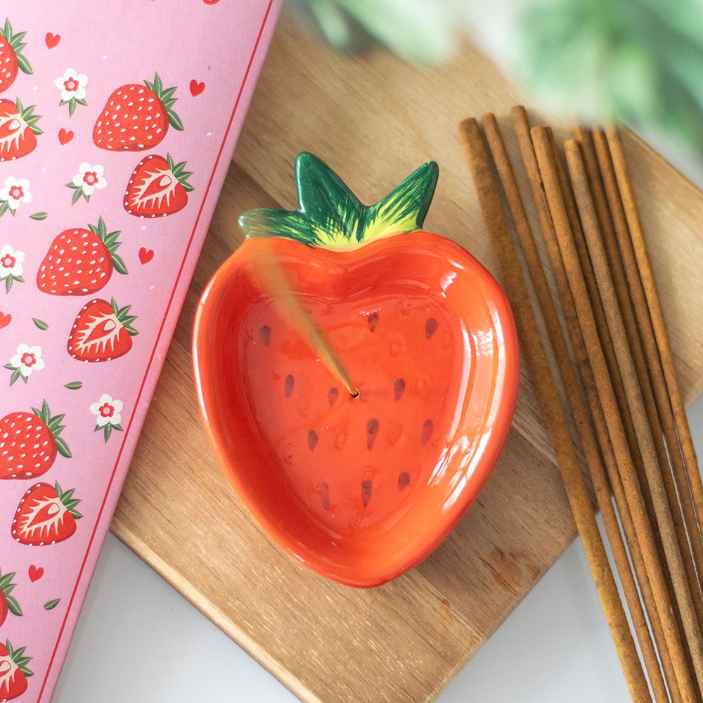 Ceramic strawberry-shaped dish with incense sticks on a wooden surface