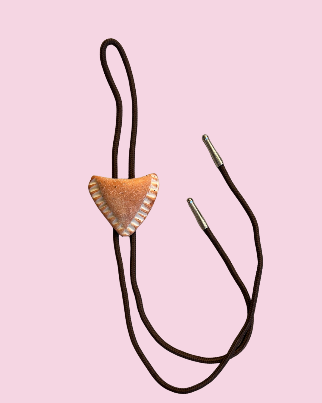 Empanada bolo tie with a brown leather strap on a pink background