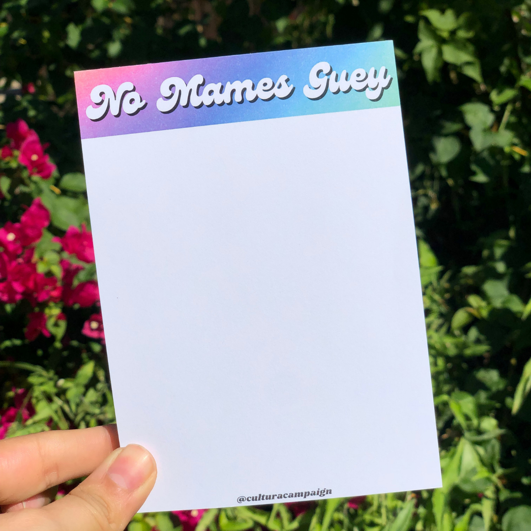 A multicolored notepad with the text 'No Mames, Guey' printed on the cover, held in a person's hand.